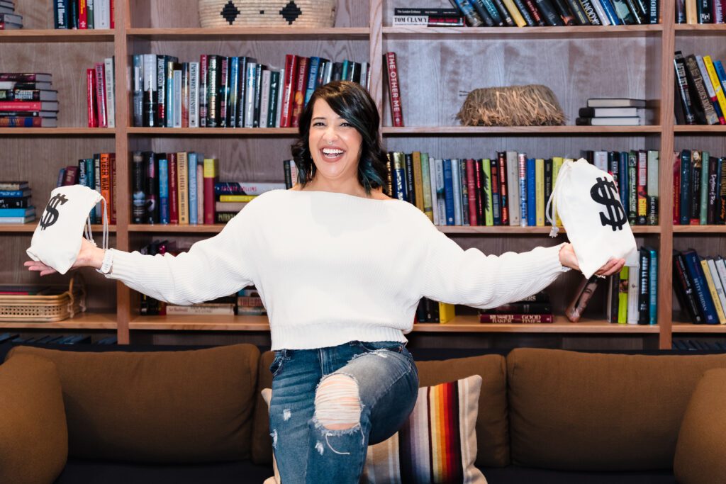 brand photo of a business coach holding two bags with a money sign, and lifting one of her legs to illustrate the balance in finances.