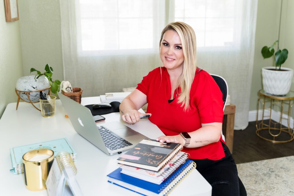 brand photo of a coach sitting in her home office, pen in the hand and laptop at the desk
