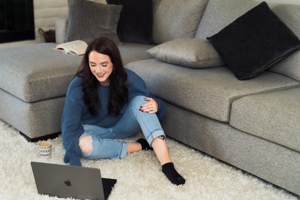 brand photo of a woman sitting on the living room rug with a laptop 