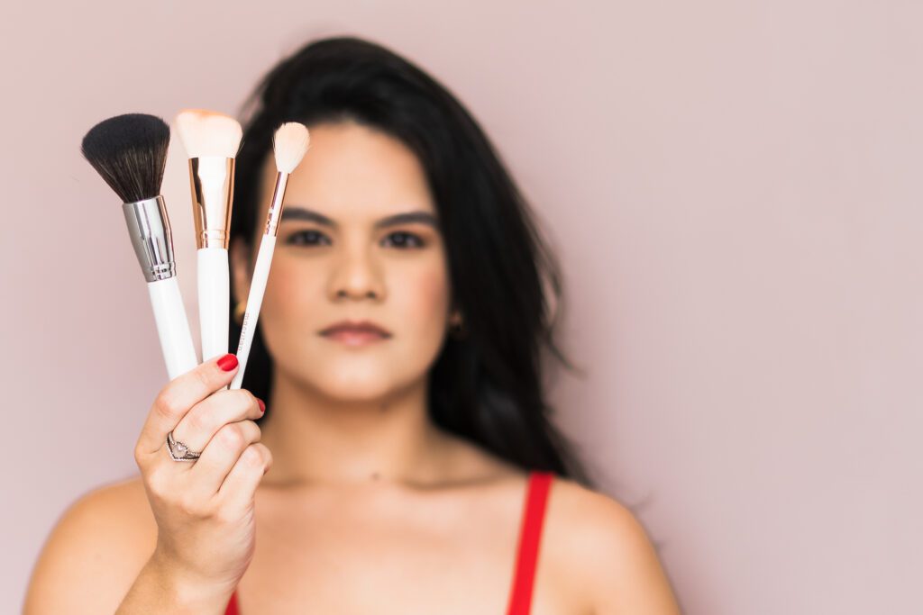 brand photo of a make up artist holding make up brushes in front of her face