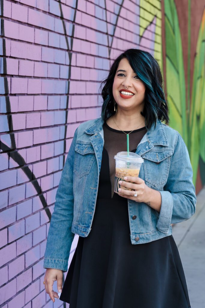 woman walking close to a colorful mural, holding a cup of coffee