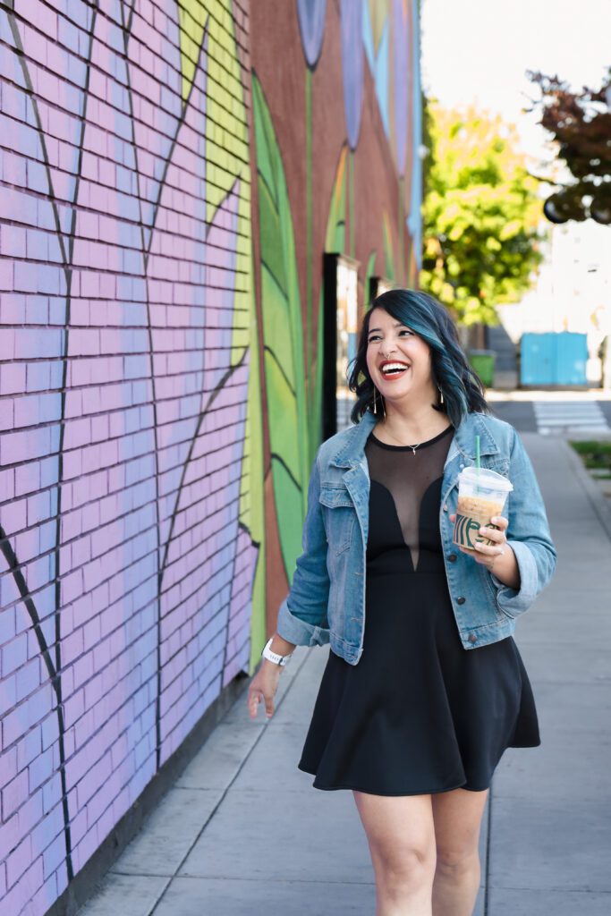 brand photo of a female entrepreneur walking in the street close to a colorful mural, holding a Starbucks Coffee
