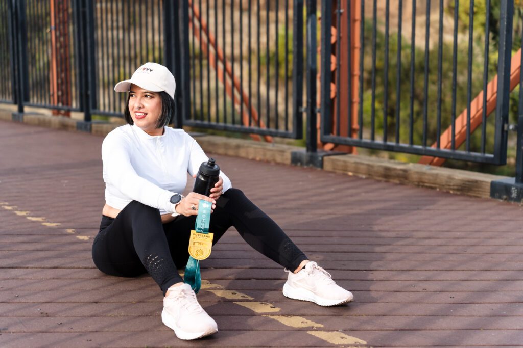 woman wearing a workout outfit posing sit holding a marathoner medal 