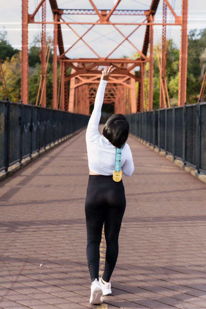 brand photo of the back of a marathoner celebrating her achievement holding her medal and making a peace sign.