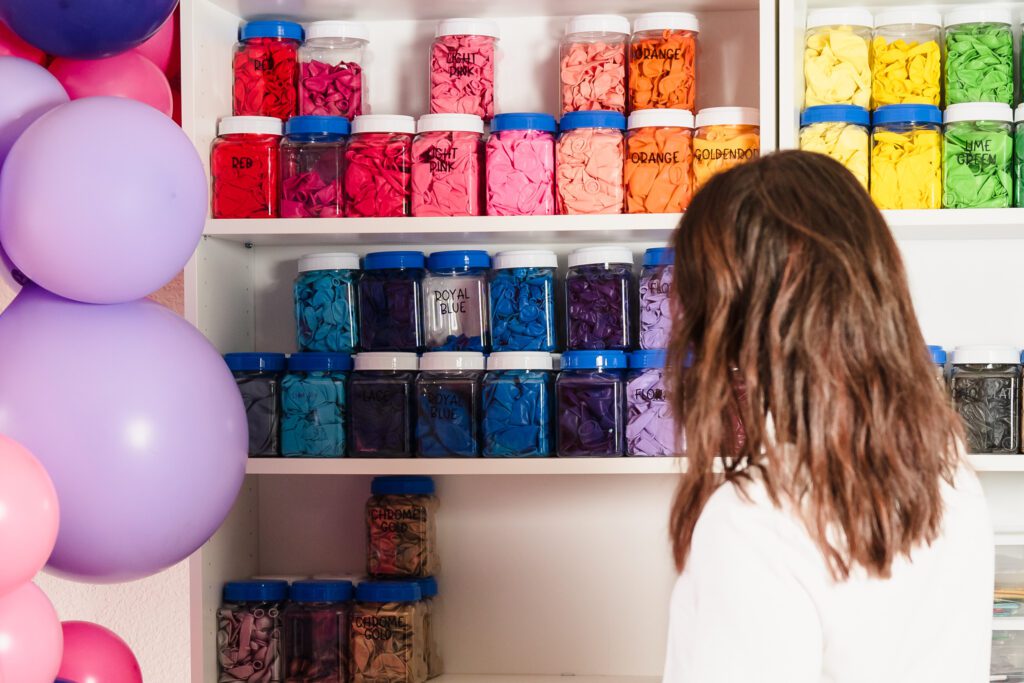 brand photo of a balloon business owner looking at a shelf of balloon containers