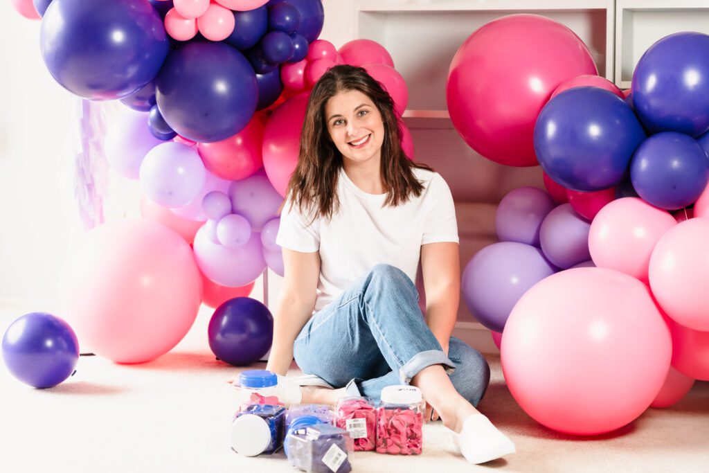 woman sit in the floor among a lot of pink and purple balloons