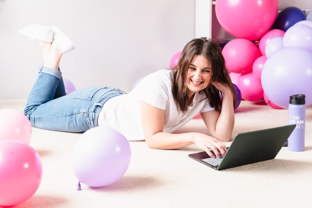 brand photo of a business owner lying in the floor with her laptop and balloons