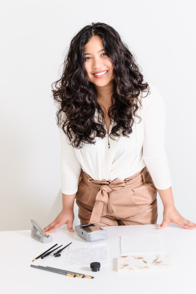 lifestyle headshot of a calligrapher leaning on the desk with her tools of the trade