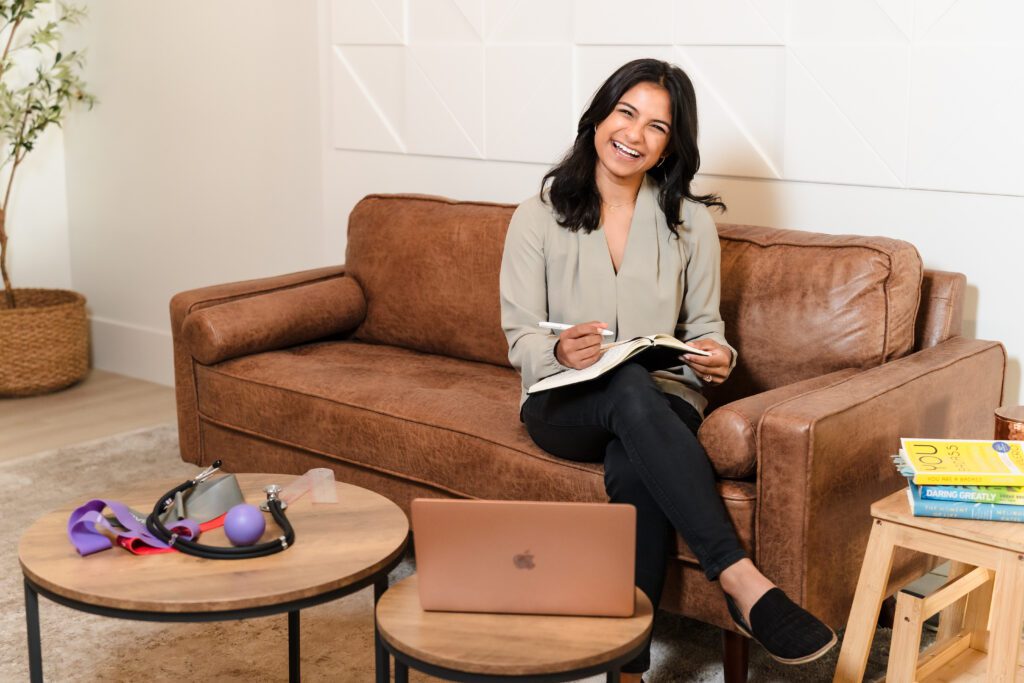 physical therapist posing seating in the couch, notebook in her lap and smiling 