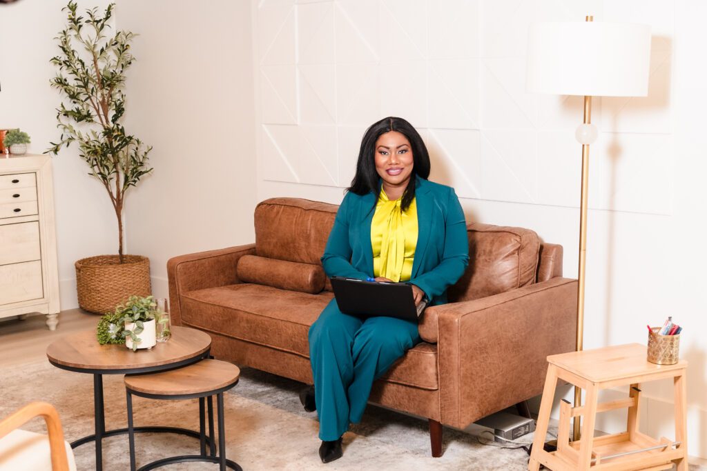 woman posing seated in the couch holding a laptop, looking at the camera